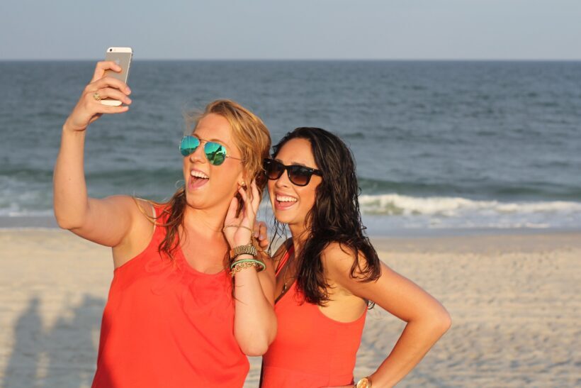 Amigas sonriendo en la playa frente al móvil